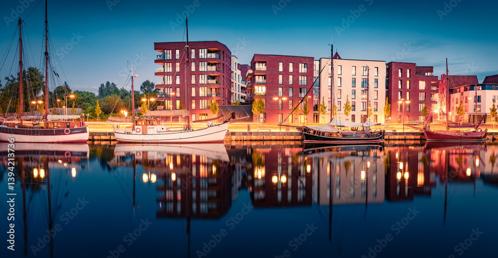 Night summer view of illuminated building and white motorboats on the shore of Ryck river. Amazing evening cityscape of Greifswald town, Germany, Europe. Calm summer scene of Ryck river.