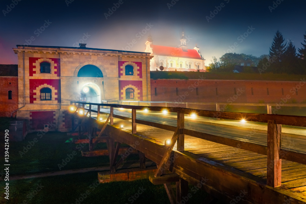 Night summer view of fortress and city of Zamosc. Illuminated morning scene of walls of fortress and Szczebrzeska Gate with Cathedral of Resurrection and Saint on background, Zamosc. Poland, Europe.