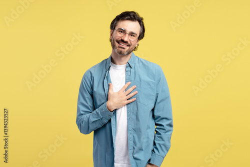 Grateful man keeping hand on chest and smiling on yellow background