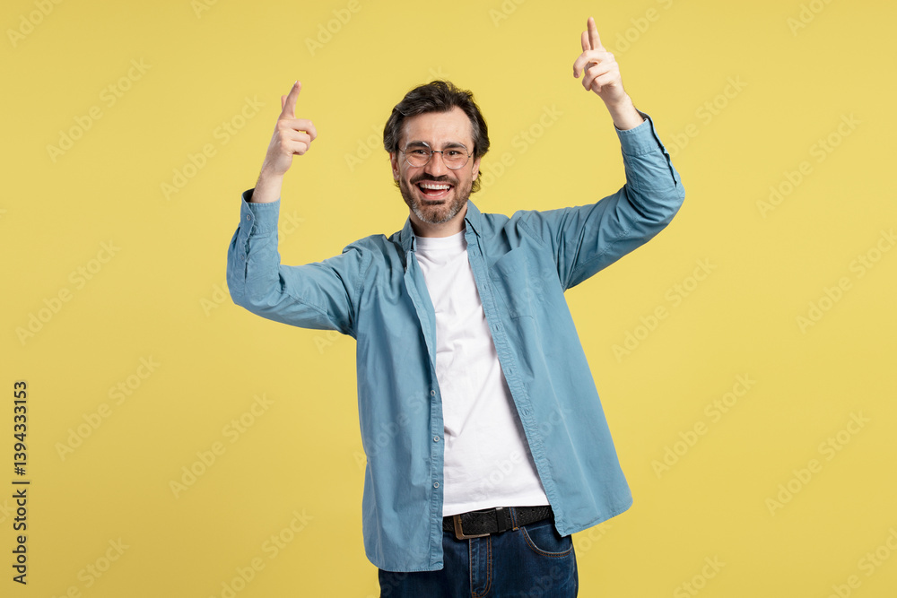 Enthusiastic man pointing up with index fingers on yellow background Enthusiastic man pointing up with index fingers on yellow background