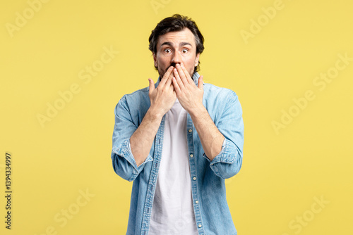 Shocked man covering his mouth with hands on yellow background