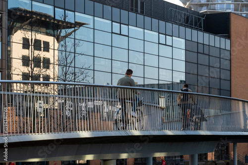 Cyclists crossing sky bridge with reflections of city buildings, urban mobility in Copenhagen