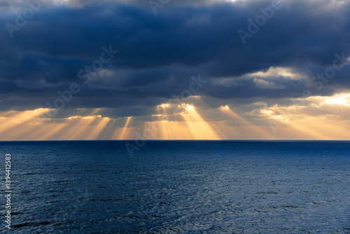 Yellow sunbeams breaking through the clouds over the ocean