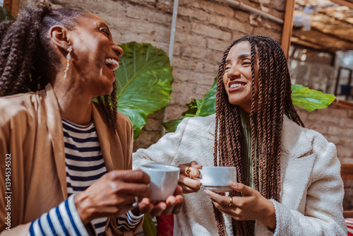 Two cheerful black women sharing a moment of laughter and connection over coffee in a stylish cafe.