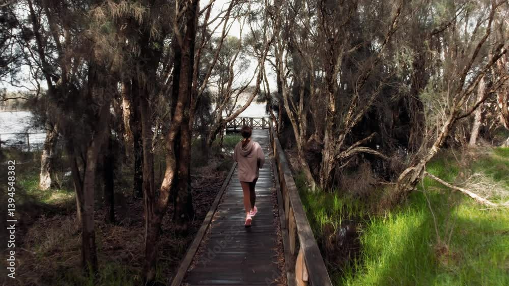 Rear view of a person is jogging on a wooden path surrounded by lush greenery and trees Rear view of a person is jogging on a wooden path surrounded by lush greenery and trees
