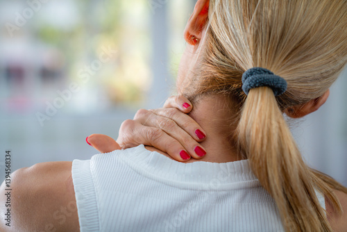 Neck pain is indicated by a woman rubbing her neck with her hand. Her fingers target the sore muscles, reflecting discomfort, showcasing the physical stress and pain management.