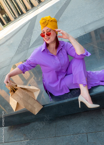 woman with craft shopping bags in the city. The concept of fashionable Consumerism and ecology. An adult Asian woman in a purple suit with red and yellow accents enjoys shopping . a sunny day.