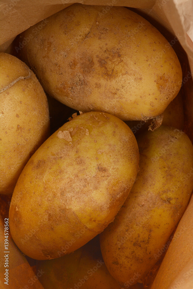 A close-up shows several unpeeled potatoes with slightly textured, light brown skin inside a brown paper bag A close-up shows several unpeeled potatoes with slightly textured, light brown skin inside a brown paper bag