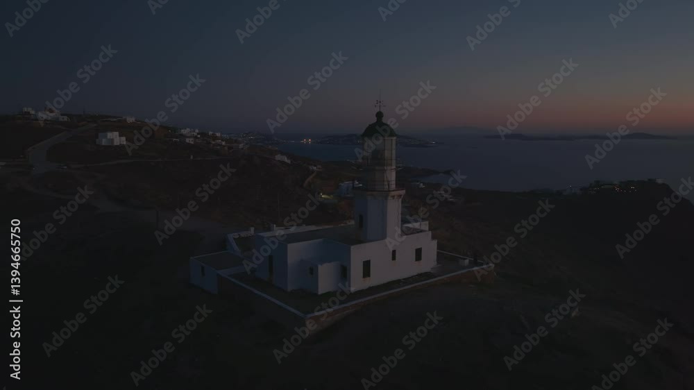 The Armenistis Lighthouse in Mykonos is captured at twilight, just as its light turns on. The sky transitions from blue to deep hues while the lighthouse begins to glow, creating a peaceful atmosphere The Armenistis Lighthouse in Mykonos is captured at twilight, just as its light turns on. The sky transitions from blue to deep hues while the lighthouse begins to glow, creating a peaceful atmosphere