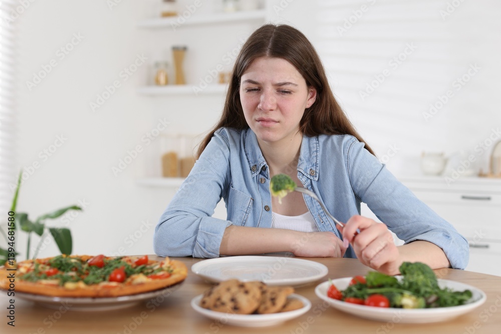 Sad teen girl holding fork with broccoli at home. Eating disorder Sad teen girl holding fork with broccoli at home. Eating disorder