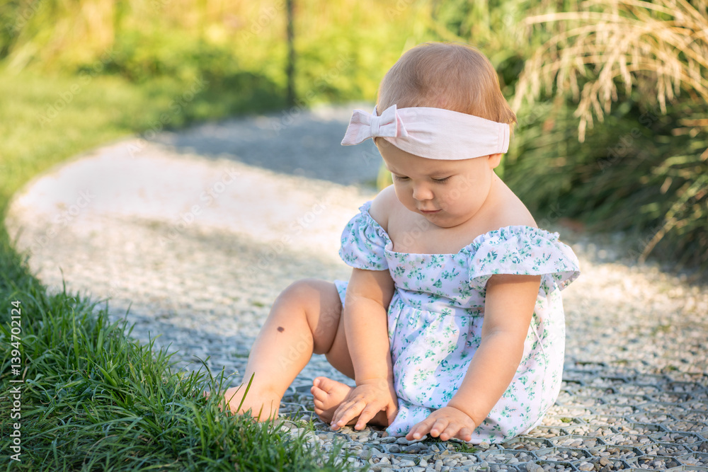 Cute adorable baby girl in dress sitting on ground in park outdoors. 12-18 month toddler having fun on summer day, happy childhood Cute adorable baby girl in dress sitting on ground in park outdoors. 12-18 month toddler having fun on summer day, happy childhood