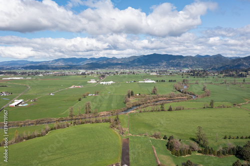 Aerial views of lush green countryside in Tillamook, Oregon, a small coastal town near the Pacific Ocean, showing farmlands, country roads, rural houses, mountains, and blue sky in spring-summer