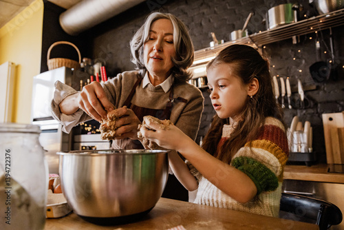 Φωτογραφία An elderly White grandmother and school-aged granddaughter in a colorful sweater bake together in a cozy kitchen