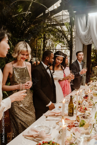 Obraz na plátně A mid-20s Black newlywed couple, chatting while standing among a diverse group o
