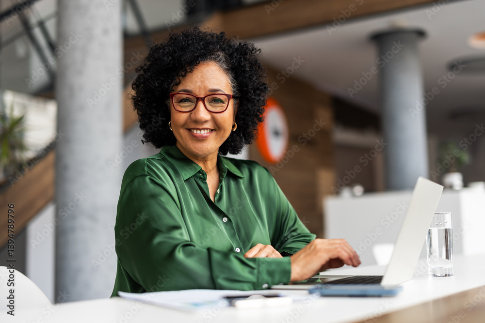 Confident Professional Woman Smiling While Working on Laptop in Modern Office