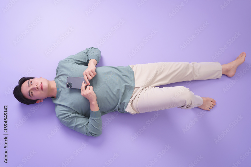 Person lying on a purple surface holding a smartphone while wearing casual clothing in a relaxed indoor setting Person lying on a purple surface holding a smartphone while wearing casual clothing in a relaxed indoor setting