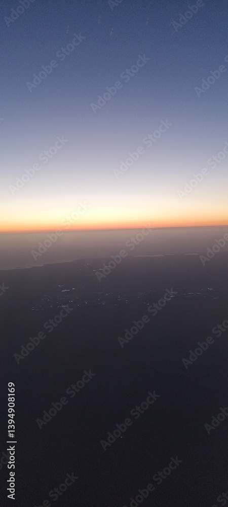 Aerial View of Dusk Horizon from Airplane. A tranquil view of the horizon at dusk from an airplane window, with soft gradient sky colors and faint city lights below Aerial View of Dusk Horizon from Airplane. A tranquil view of the horizon at dusk from an airplane window, with soft gradient sky colors and faint city lights below
