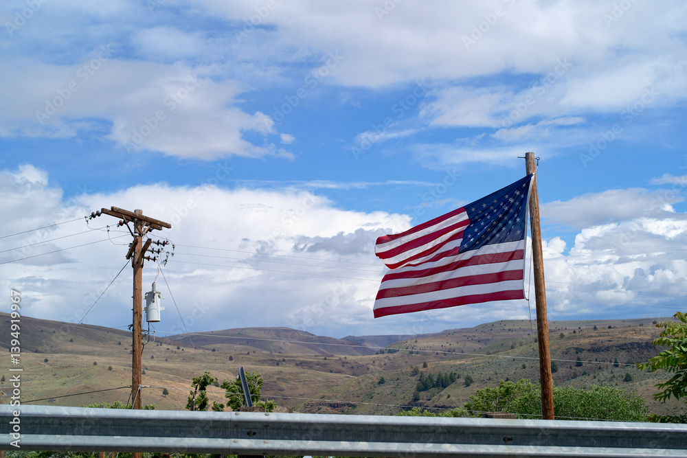 American flag waving on a pole against a vast open landscape and blue sky with clouds. Oregon, USA American flag waving on a pole against a vast open landscape and blue sky with clouds. Oregon, USA