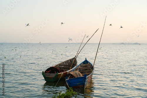 Two fishing boats with tall poles float on a calm sea under a sky with flying birds. Tanzania, Africa photo