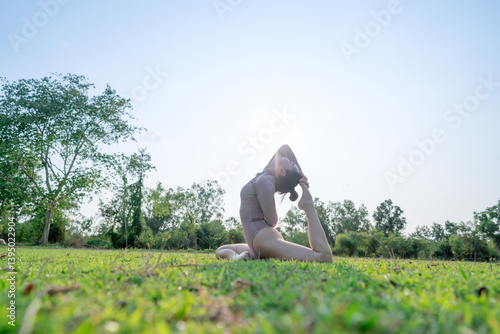 Mujer asiática haciendo yoga en el césped mientras se pone el sol. photo