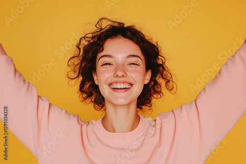 Joyful Radiance: An attractive young woman with a contagious smile and arms wide open against a vibrant yellow backdrop, conveying happiness and positivity. 