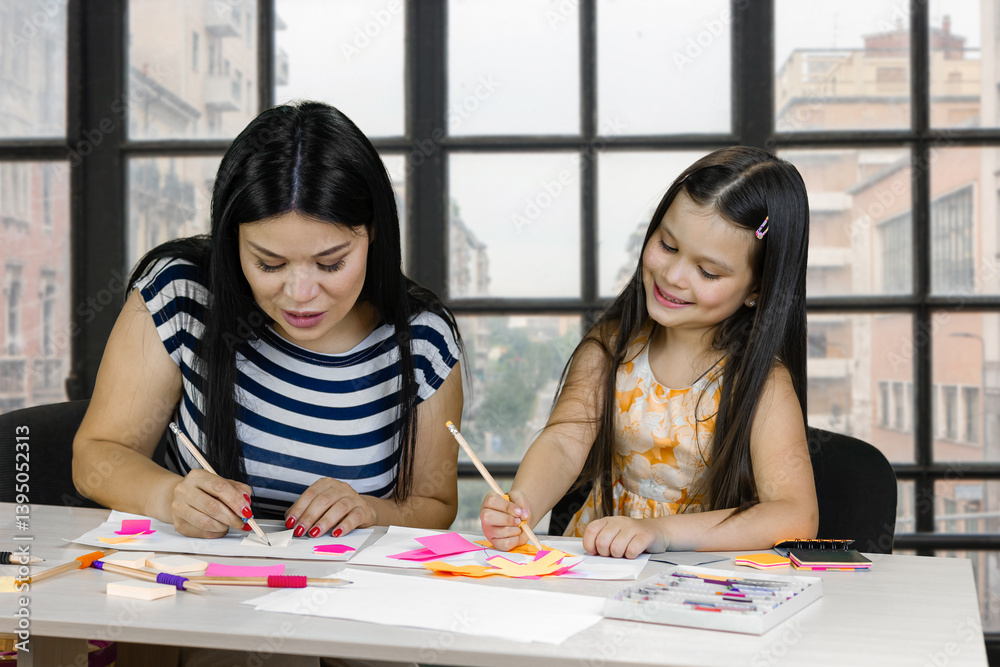 Brunette asian woman and caucasian little girl drawing something together. Checkered windows background. Brunette asian woman and caucasian little girl drawing something together. Checkered windows background.