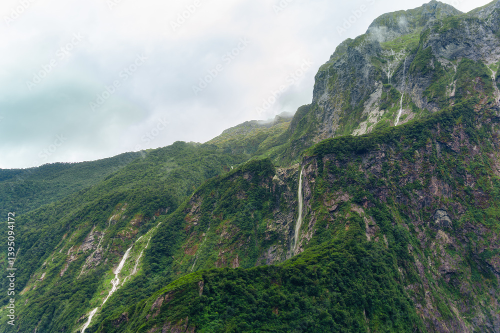 Naklejka premium Milford Sound with waterfall flowing from limestone mountain with foggy in rainforest at New Zealand