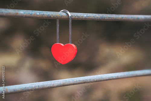 A red heart-shaped love padlock on a metal fence. Blurred background.