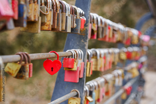 A red heart-shaped love padlock placed among many others on a fence.