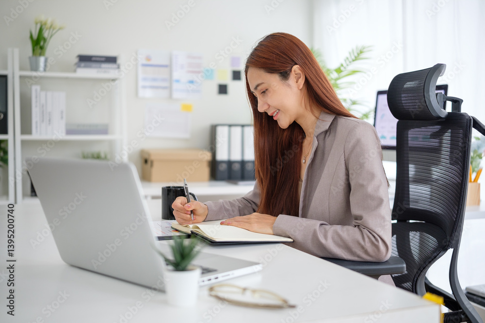 Businesswoman writing in a notebook at modern desk with a laptop in front of her. Businesswoman writing in a notebook at modern desk with a laptop in front of her.
