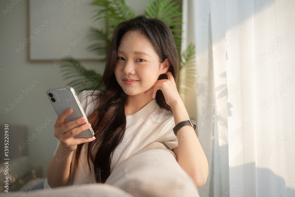 Cheerful young woman using smartphone in a bright and comfortable living room. Cheerful young woman using smartphone in a bright and comfortable living room.