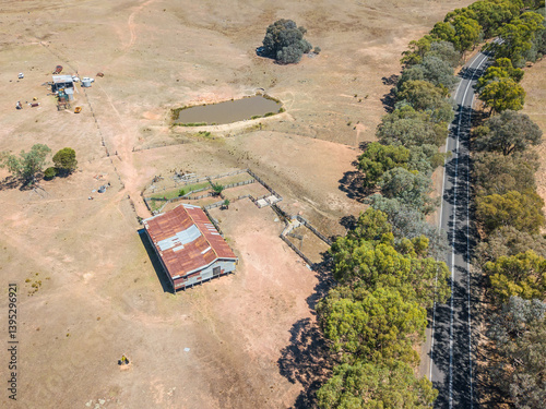 Aerial view of a shearing shed and farmland next to a tree lined road