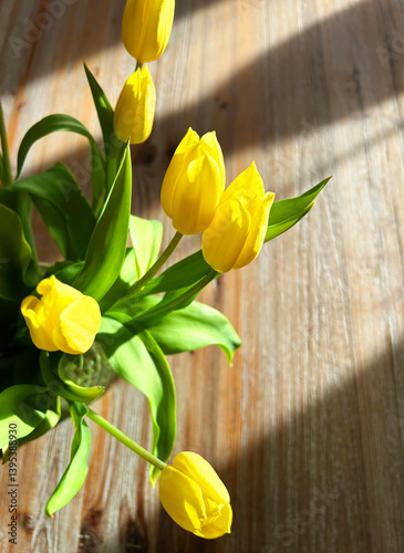 Close-up of a bouquet of sunlit yellow tulips on a rustic wooden table.