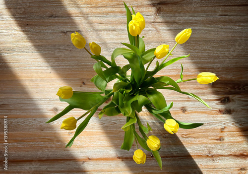 Top view of a bouquet of sunlit yellow tulips on a rustic wooden table.