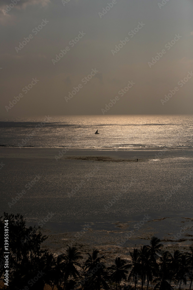 samotny, mały jacht żaglowy płynący wzdłuż rafy koralowej otaczającej lagunę, na tle wschodzącego słońca nad oceanem indyjskim, Kenia, Afryka