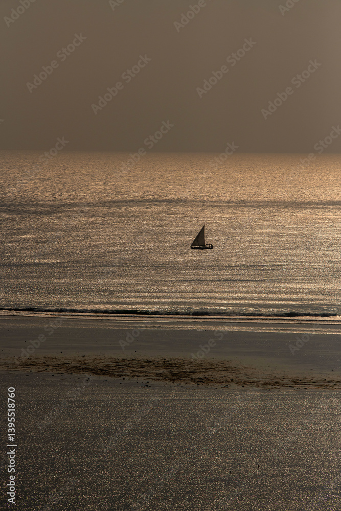 samotny, mały jacht żaglowy płynący wzdłuż rafy koralowej otaczającej lagunę, na tle wschodzącego słońca nad oceanem indyjskim, Kenia, Afryka