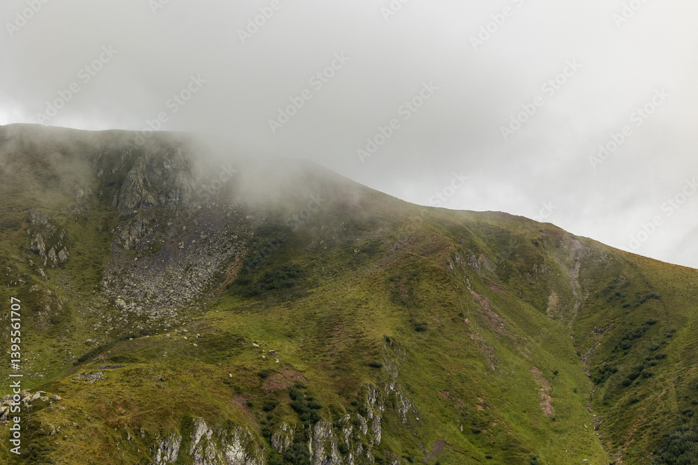 vista dettagliata sulle cime ed i pendii erbosi e rocciosi di alcune montagne alpine nel nord Italia, di giorno, coperte parzialmente dalle nuvole, in estate
