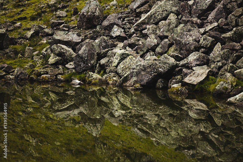 dettaglio di rocce e grandi massi che si riflettono sulla superficie piatta di un lago di montagna