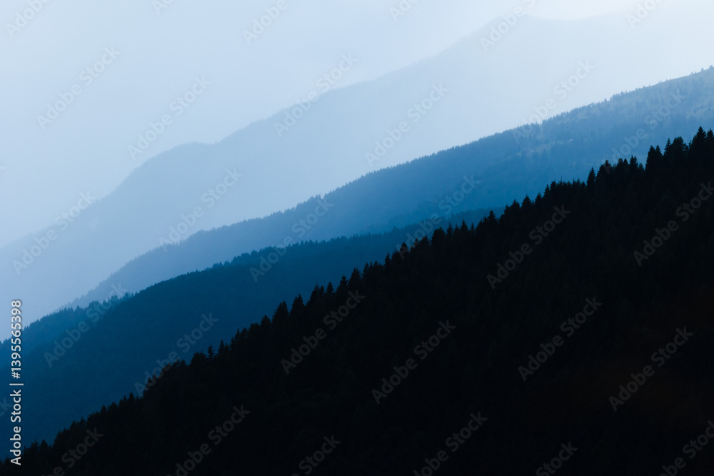 sagome di pendii di varie montagne in controluce, colorate da sfumature di blu ed avvolte nella foschia