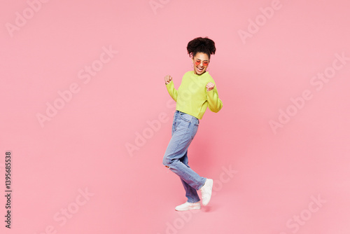 Full body side view young woman of African American ethnicity she wear green sweater casual clothes doing winner gesture celebrate clenching fists isolated on plain pink background. Lifestyle concept.