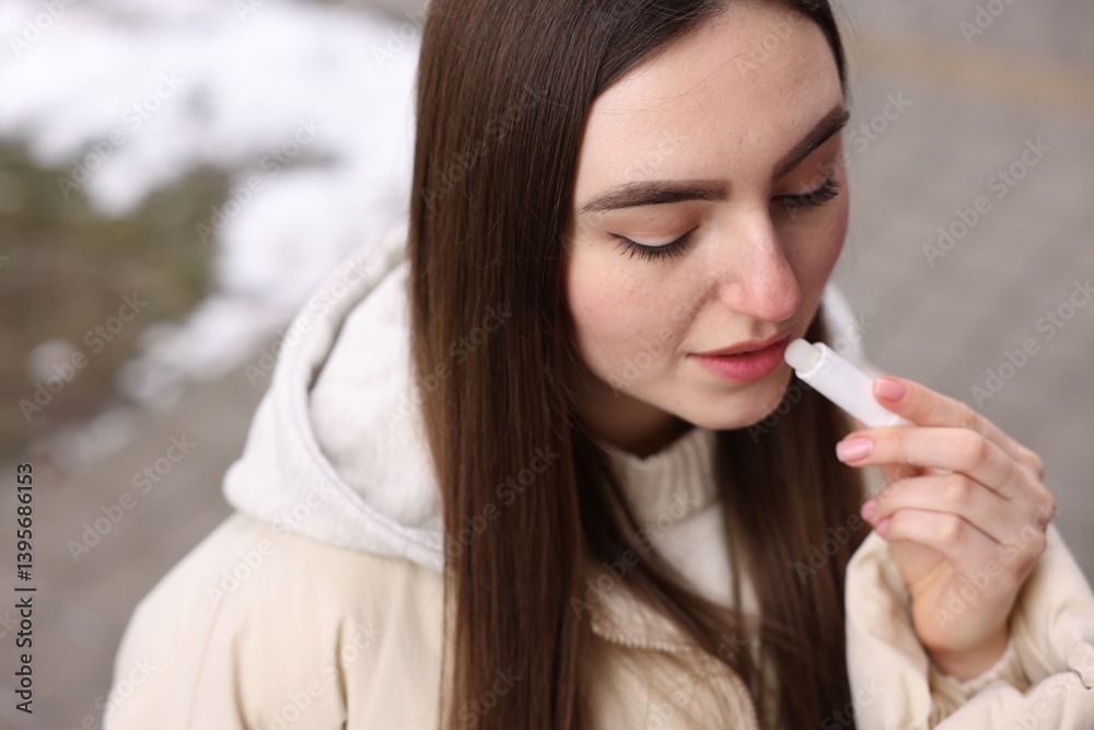 Beautiful young woman applying lip balm on winter day Beautiful young woman applying lip balm on winter day