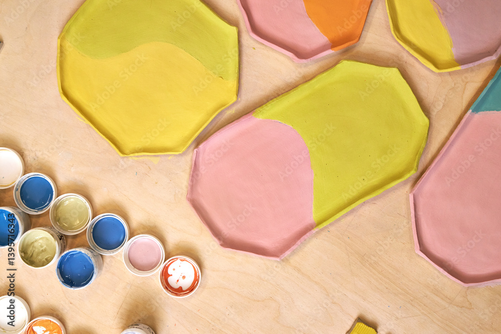 top view of handmade clay plates covered with colored glazes and glaze jars, ready for firing