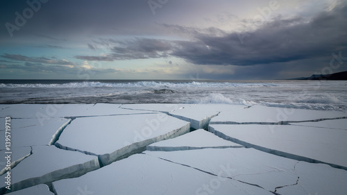 Rising waves meet cracked ice under a stormy sky, a stark reminder of sea level urgency.