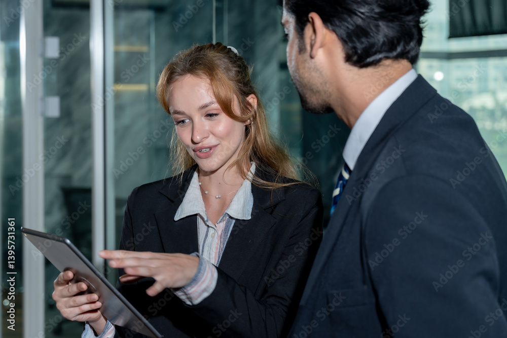 Caucasian female employee presenting idea on digital tablet to Middle Eastern male colleague during office collaboration both smiling and standing together wearing formal business outfits in workplace Caucasian female employee presenting idea on digital tablet to Middle Eastern male colleague during office collaboration both smiling and standing together wearing formal business outfits in workplace