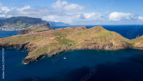View of rugged coastline and lush hills surrounding a serene bay on a sunny day in Madeira Island, Portugal