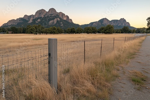 Wire fence protecting ranch at sunset with granite mountain in background