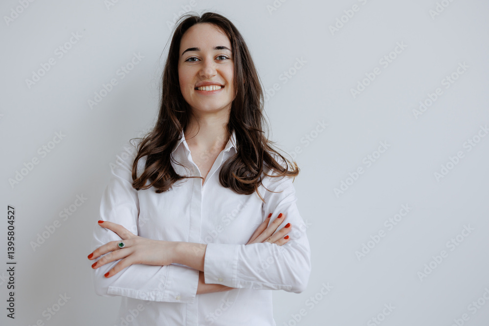 Smiling woman posing confidently with arms crossed in a bright, minimalist indoor setting, dressed in a white shirt Smiling woman posing confidently with arms crossed in a bright, minimalist indoor setting, dressed in a white shirt