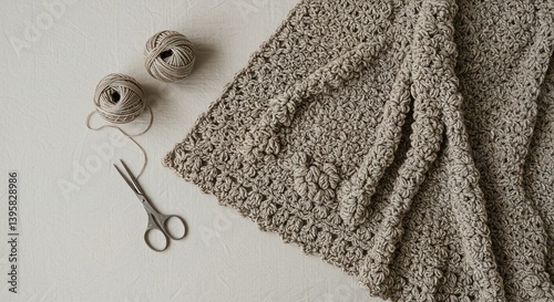 Beige crochet blanket with yarn balls and scissors on white surface