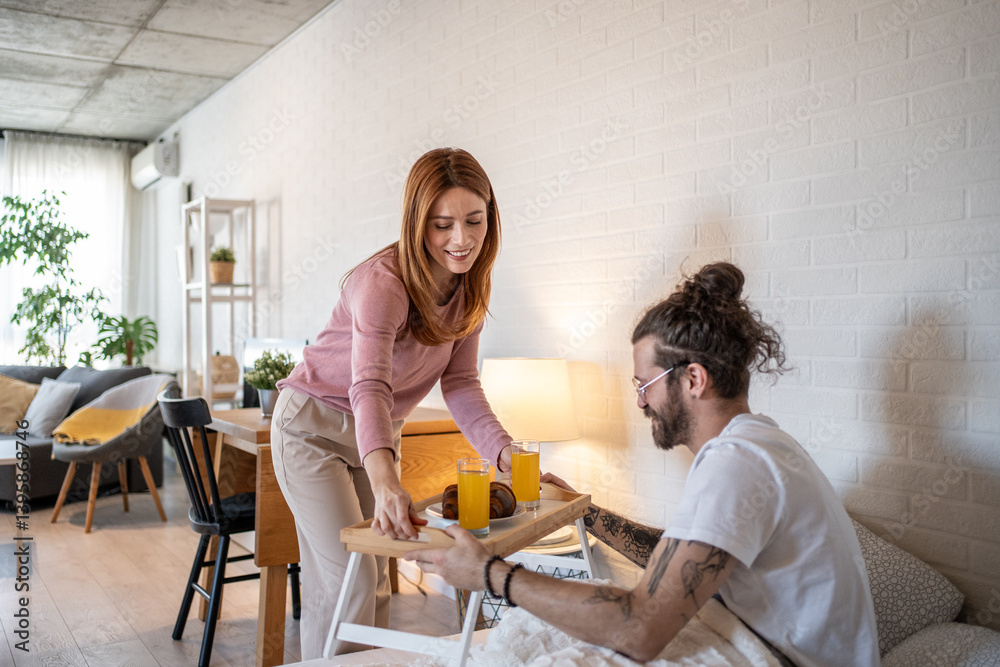 Woman bringing breakfast in bed to her husband in cozy apartment Woman bringing breakfast in bed to her husband in cozy apartment