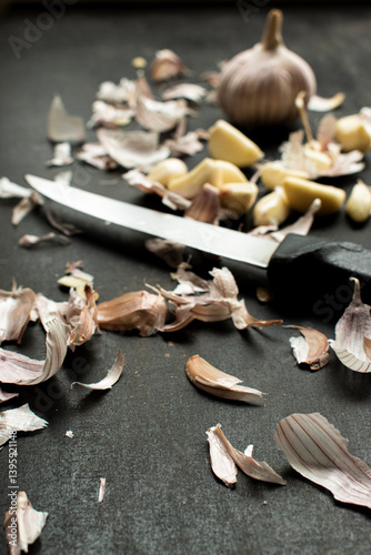Vertical shot of Garlic cloves and bulb arranged on a kitchen countertop with a knife, emphasizing cooking and ingredients. 